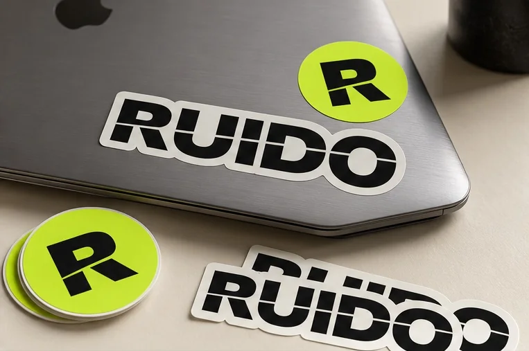 Visualización conceptual de calcomanías con el logo de RUIDO y el símbolo R sobre una notebook.